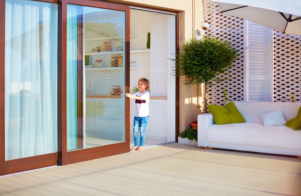Small boy pulling sliding glass door on sunny porch